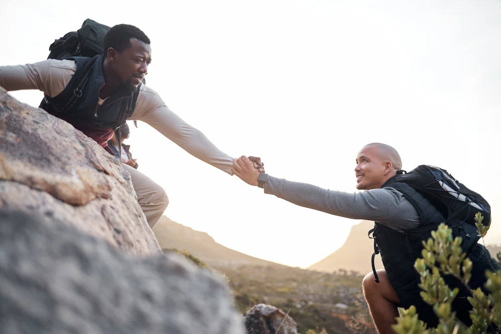 Young person helping his friend along a mountain during their hike