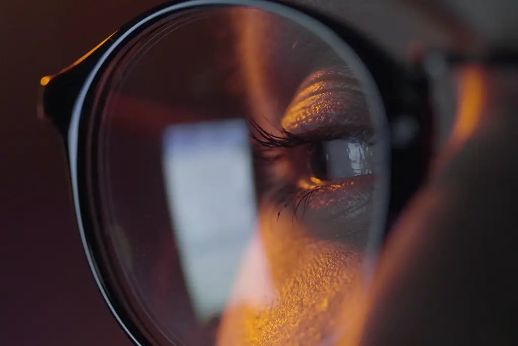 Close-up of eyeglasses reflecting a phone screen